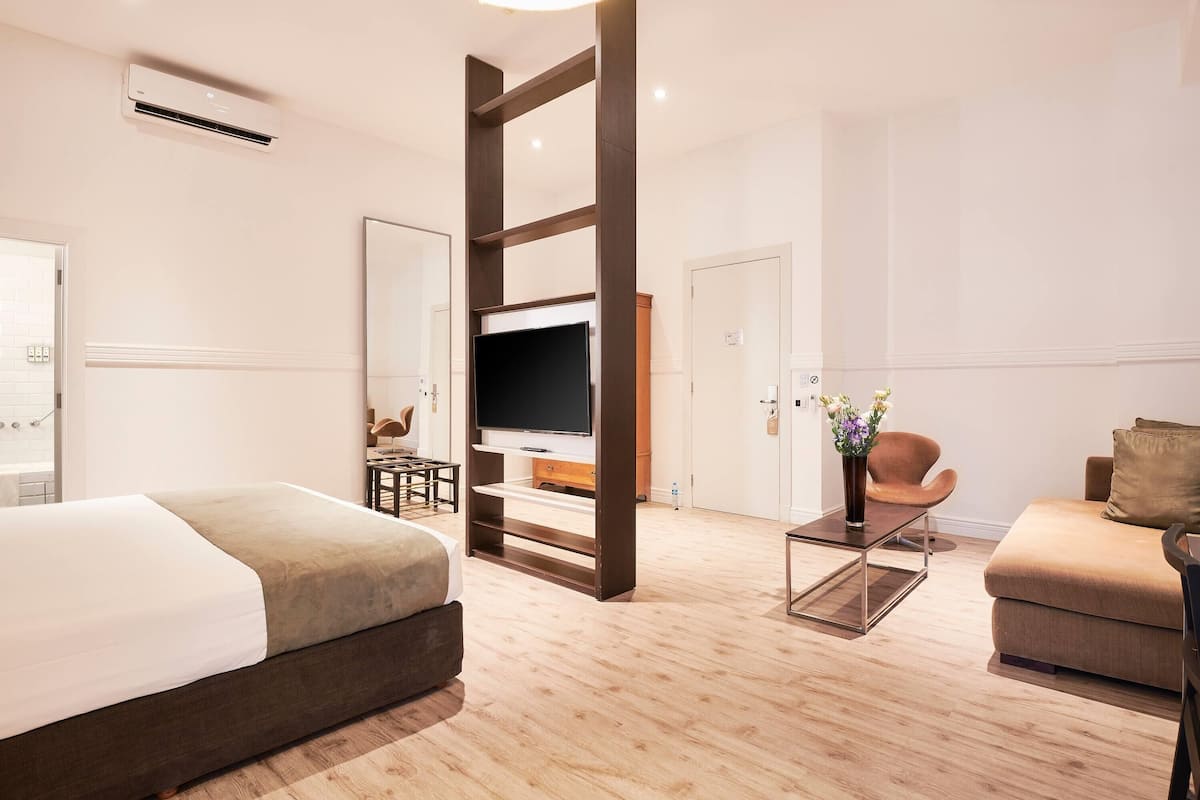 A modern hotel room with a bed, a TV, a sofa, and a desk.