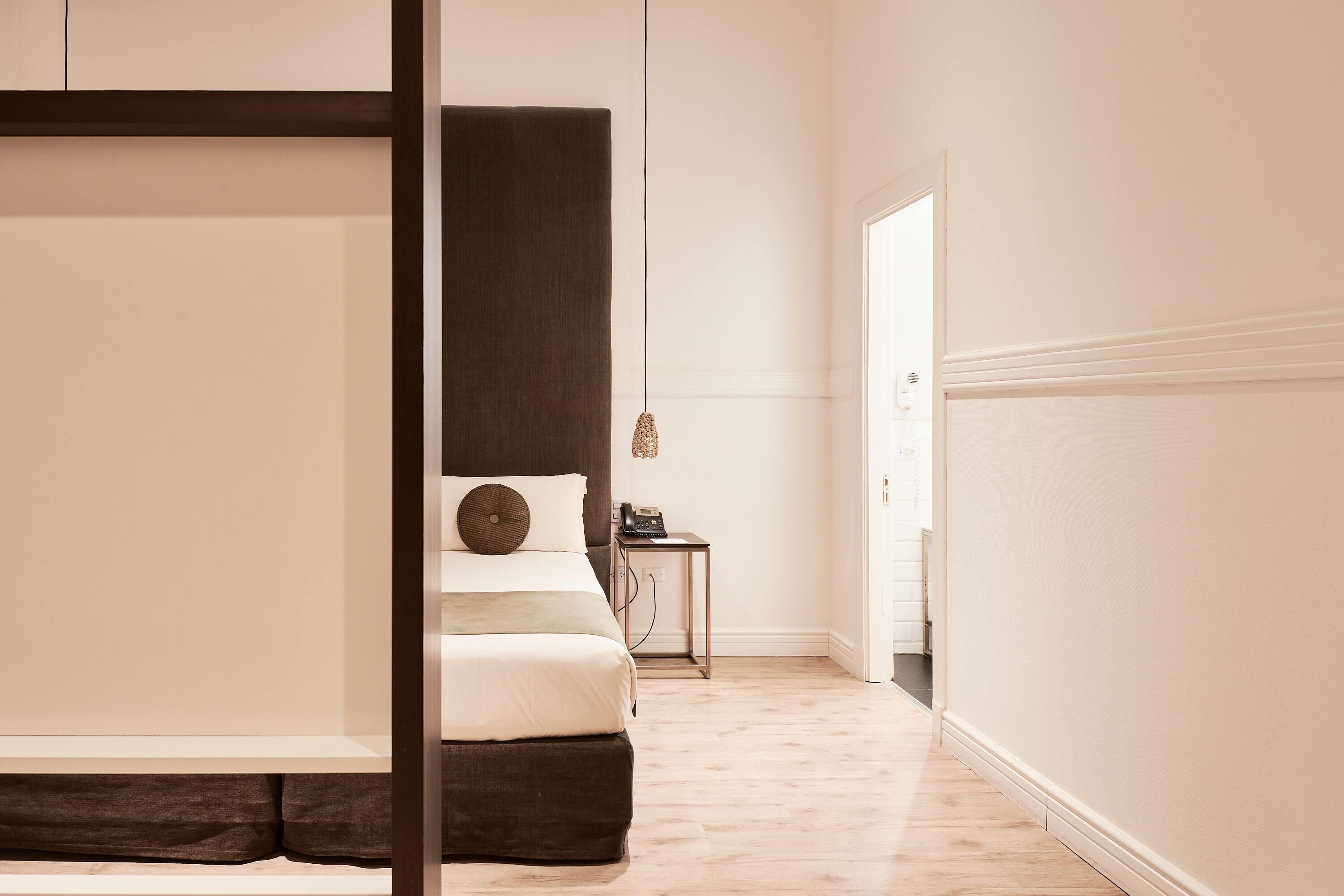 A minimalist bedroom with a large bed, bedside table, and a small table with a telephone.