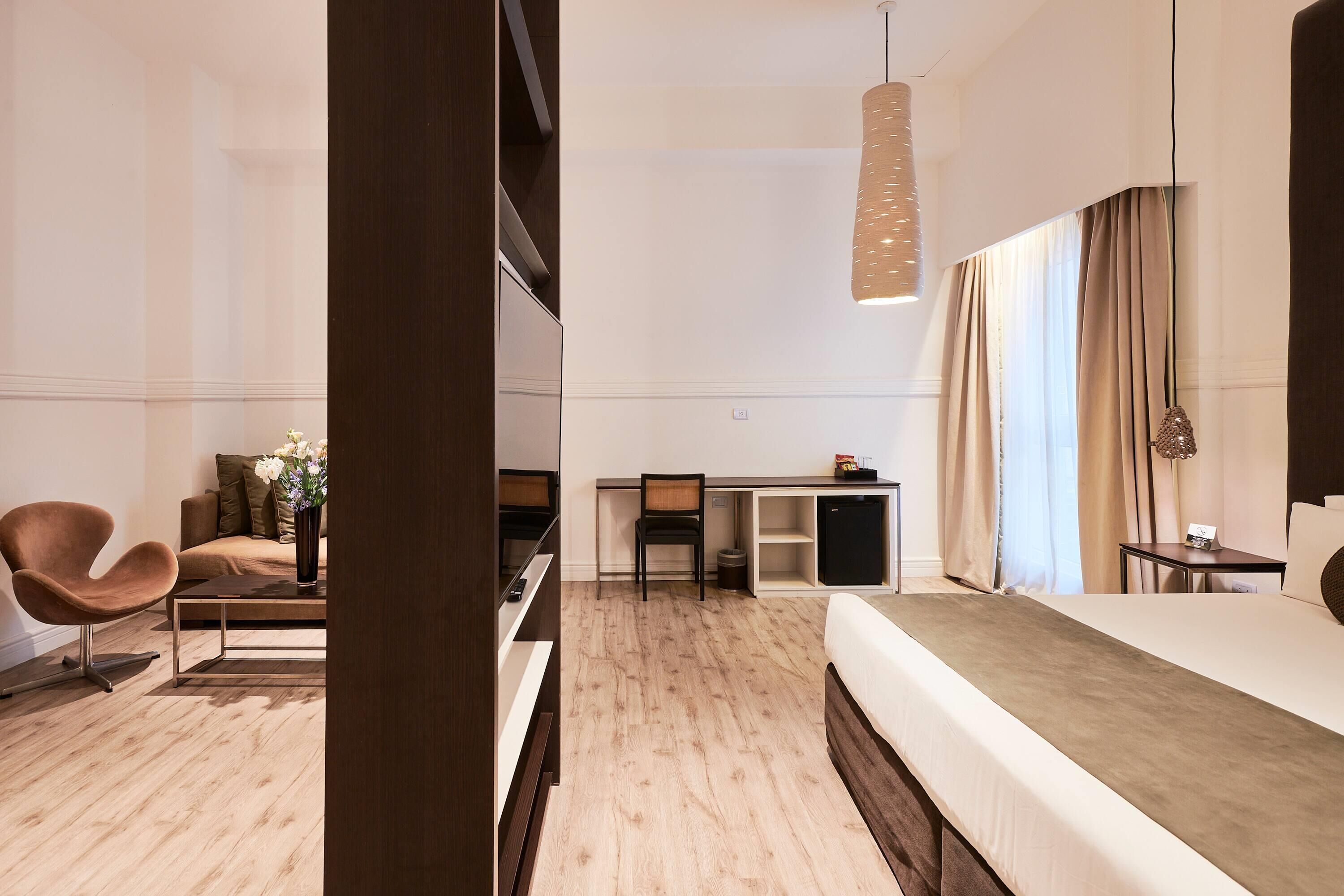 A modern hotel room with a bed, a desk, a chair, and a sofa.