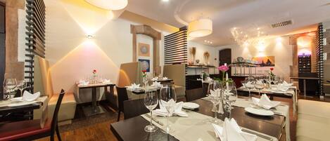 A restaurant with multiple dining tables set for guests, featuring white tablecloths, neatly arranged cutlery, and wine glasses.