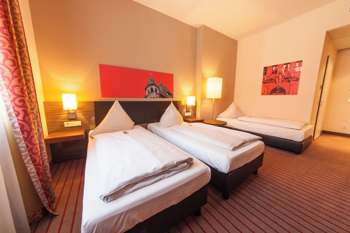 A hotel room with two single beds, a wooden headboard, a red abstract painting, two bedside lamps, and a striped carpet.