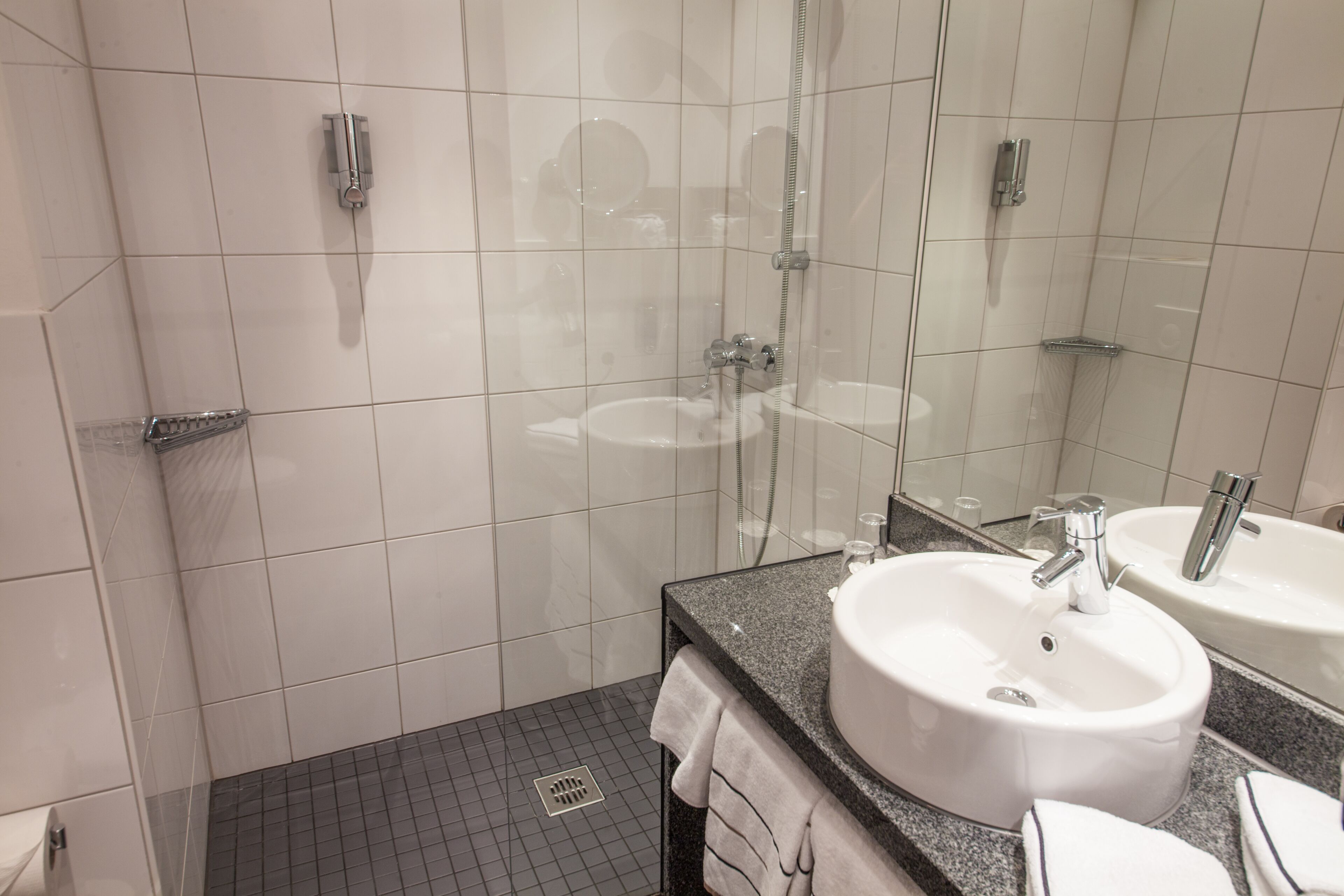 Un baño moderno con ducha de vidrio, dos lavamanos y un espejo grande.