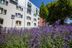 A multi-story building with balconies, a tree, and purple flowers in the foreground. - NOVINA HOTEL Tillypark (Nuremberg)