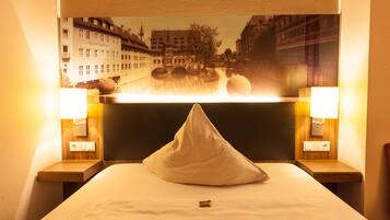 Habitación de hotel con cama, almohada, dos lámparas de noche y un cuadro colgado en la pared con vista a un paisaje urbano.