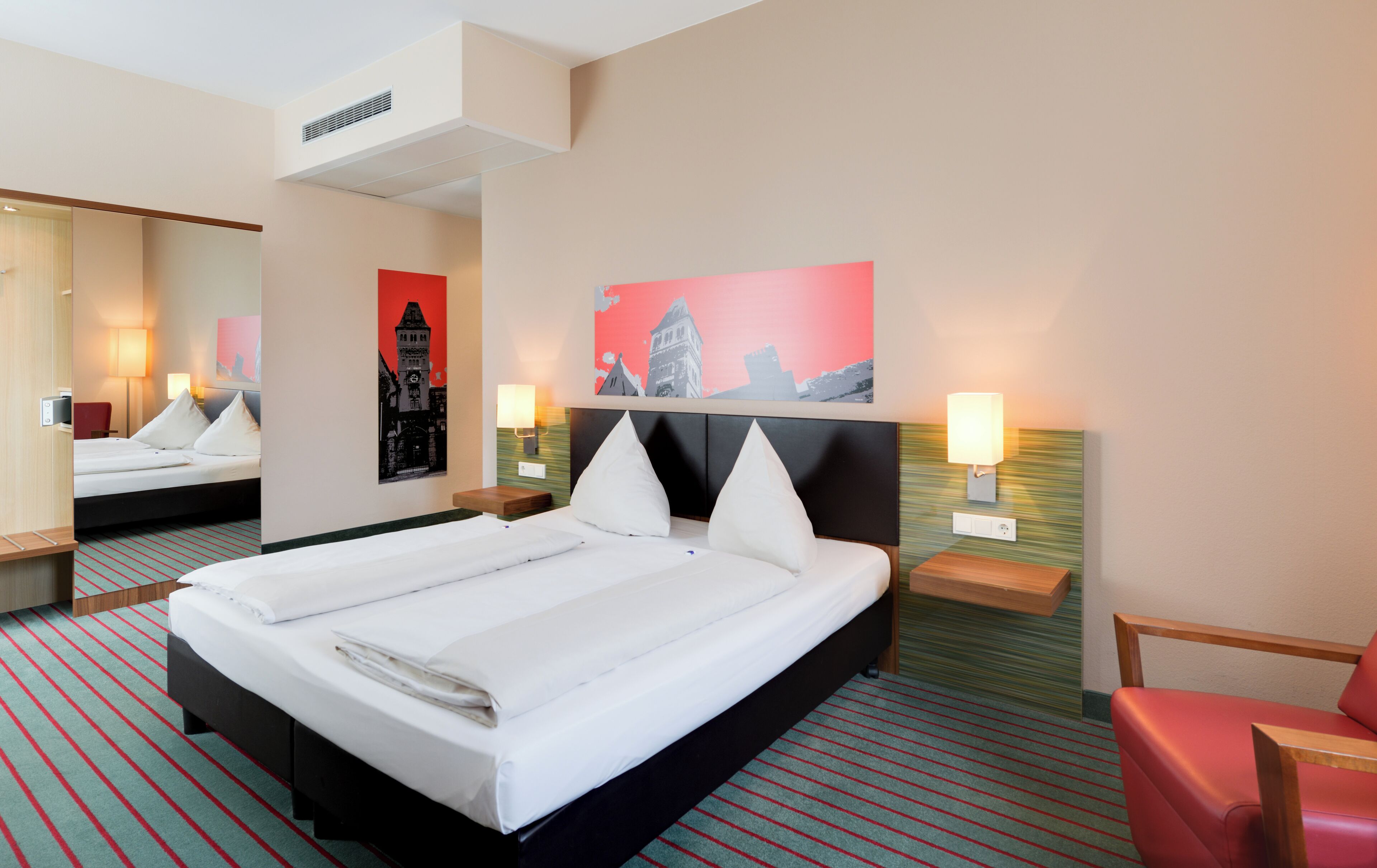 A hotel room with a large bed, two bedside tables, a mirror, and two wall-mounted lamps.