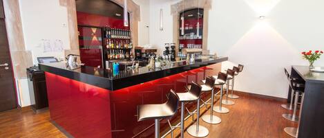 A modern bar area with a red countertop, multiple stools, and a variety of bar tools and bottles.