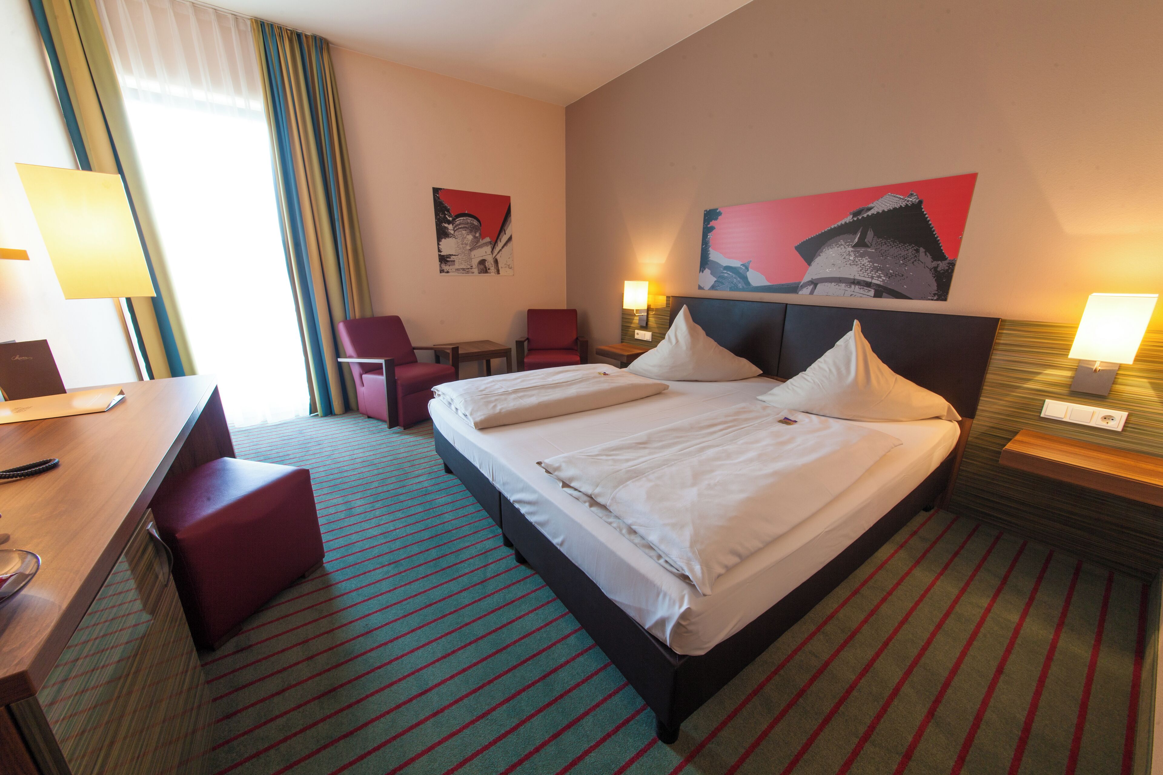 Een hotelkamer met een bed, twee stoelen, een bureau en een lamp.
