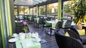 An indoor dining area with tables set for service, chairs, and a large potted plant. - NOVINA HOTEL Tillypark (Nuremberg)