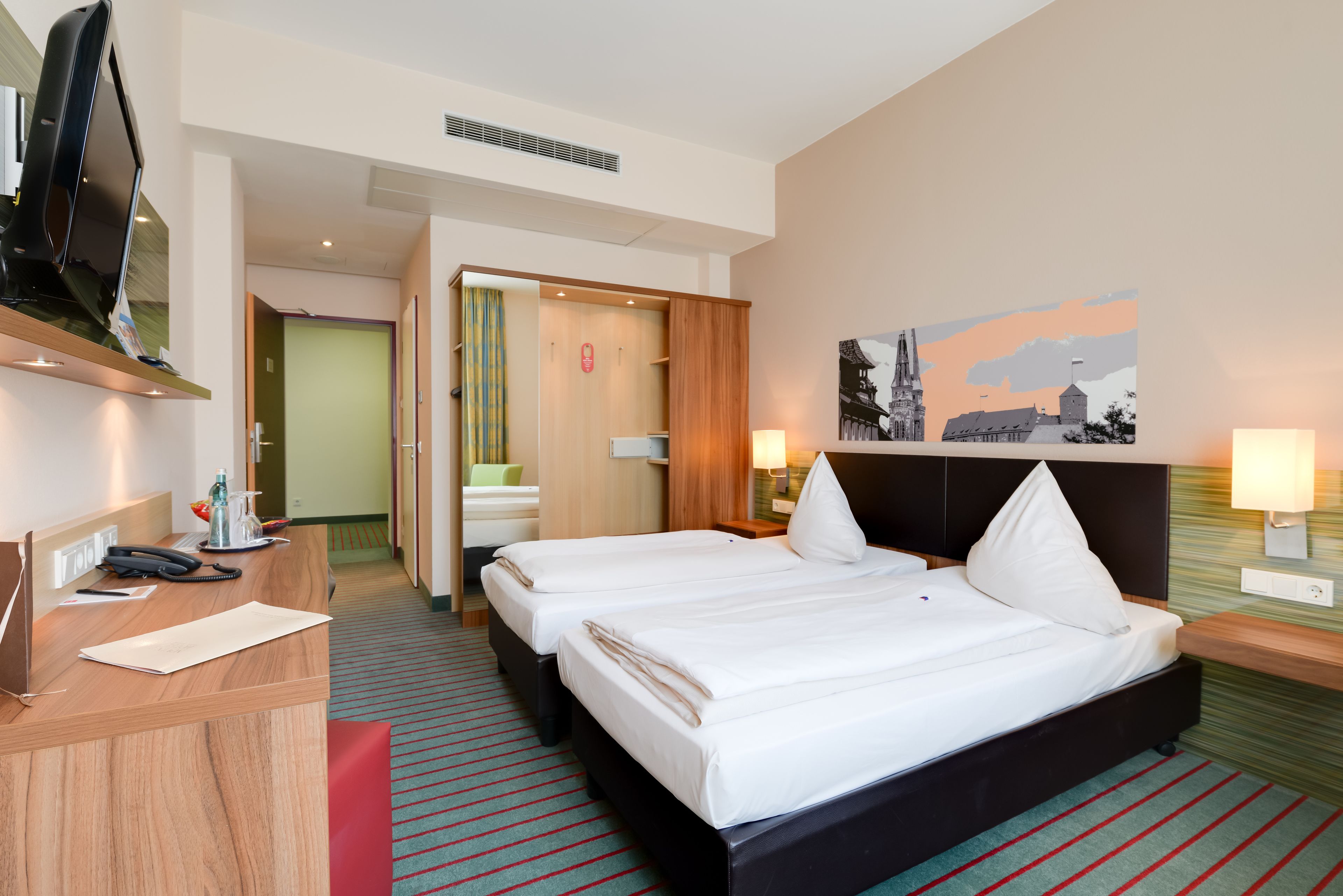 A hotel room with two beds, a desk with a telephone, a television, and a painting on the wall.