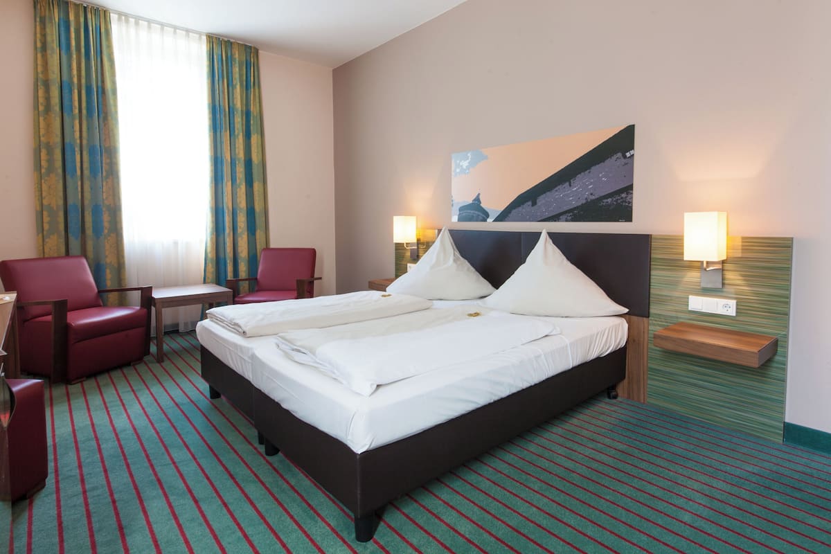 A hotel room with a large bed, two bedside tables, a desk, a chair, and a painting on the wall.
