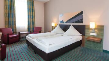 A hotel room with a large bed, two bedside tables, a desk, a chair, and a painting on the wall.