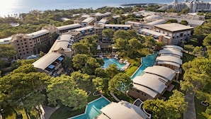 Vista aèria d'un complex turístic amb diverses edificacions, una piscina central i vegetació als voltants.