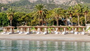 Un complex turístic a la vora de la platja, amb palmeres, parasols i una muntanya de fons.