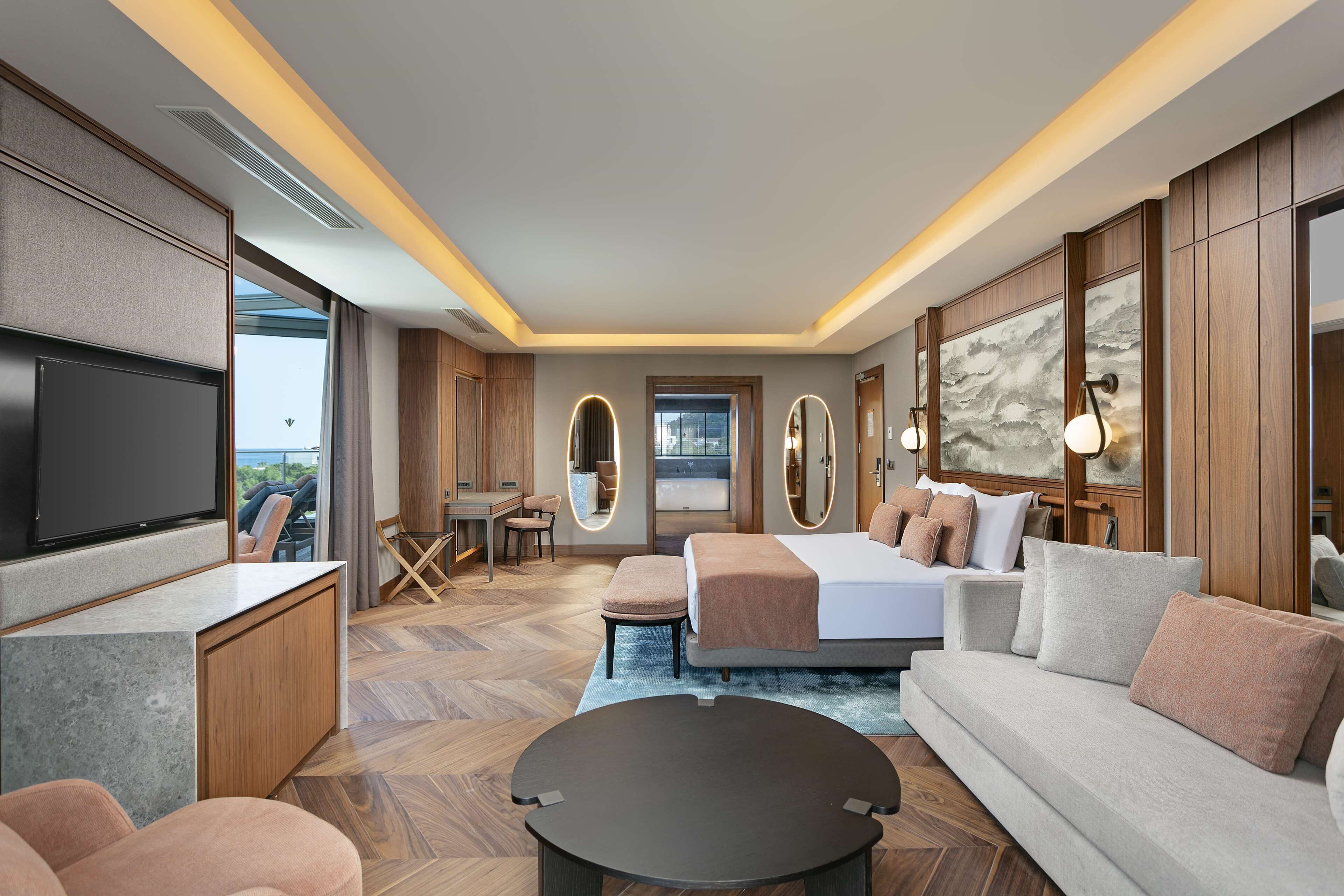 A modern hotel room with a flat-screen TV, a sofa, a bed, a desk, and a large window.