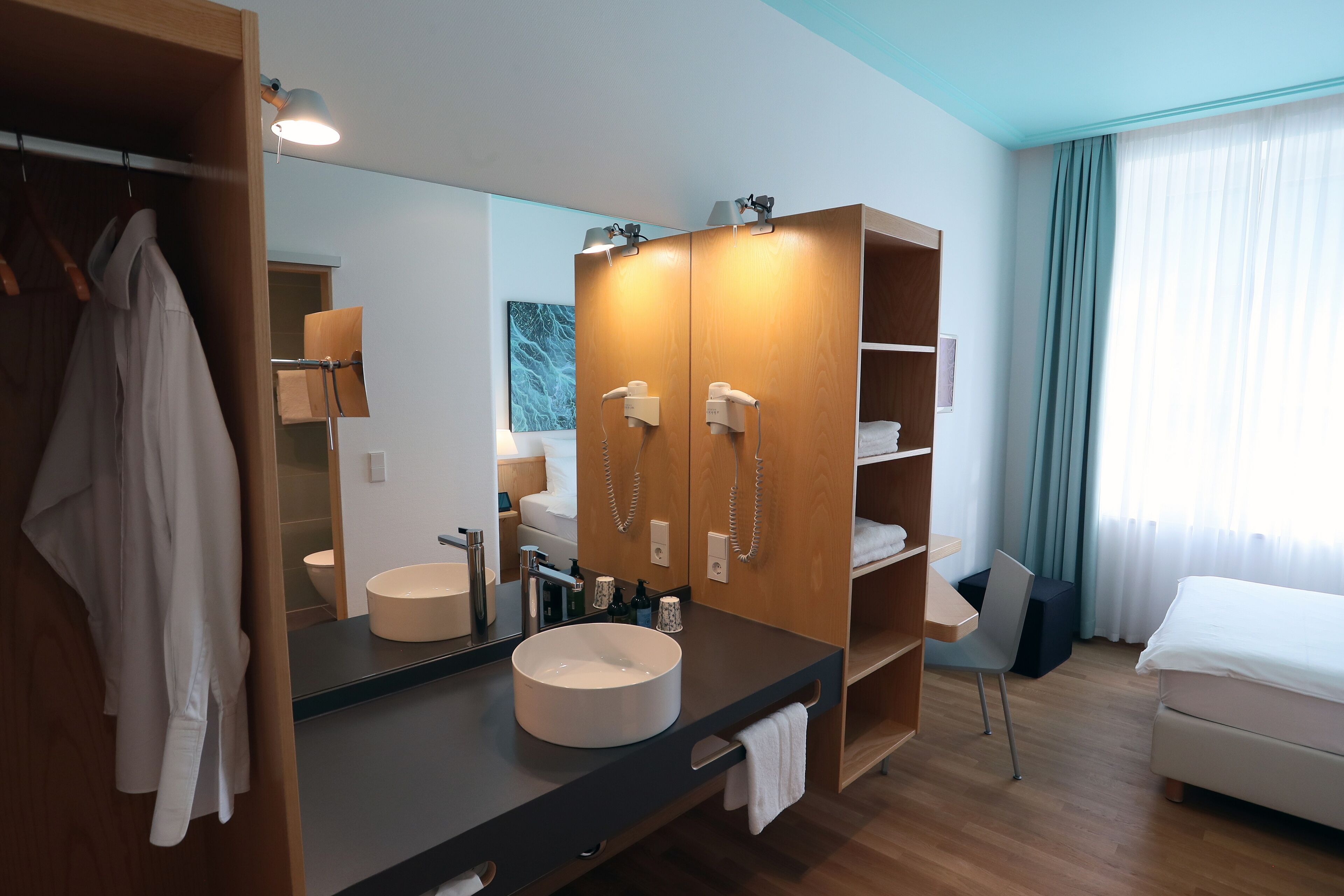 Une chambre d’hôtel moderne avec un grand miroir, une armoire en bois, un lavabo rond et un lit.