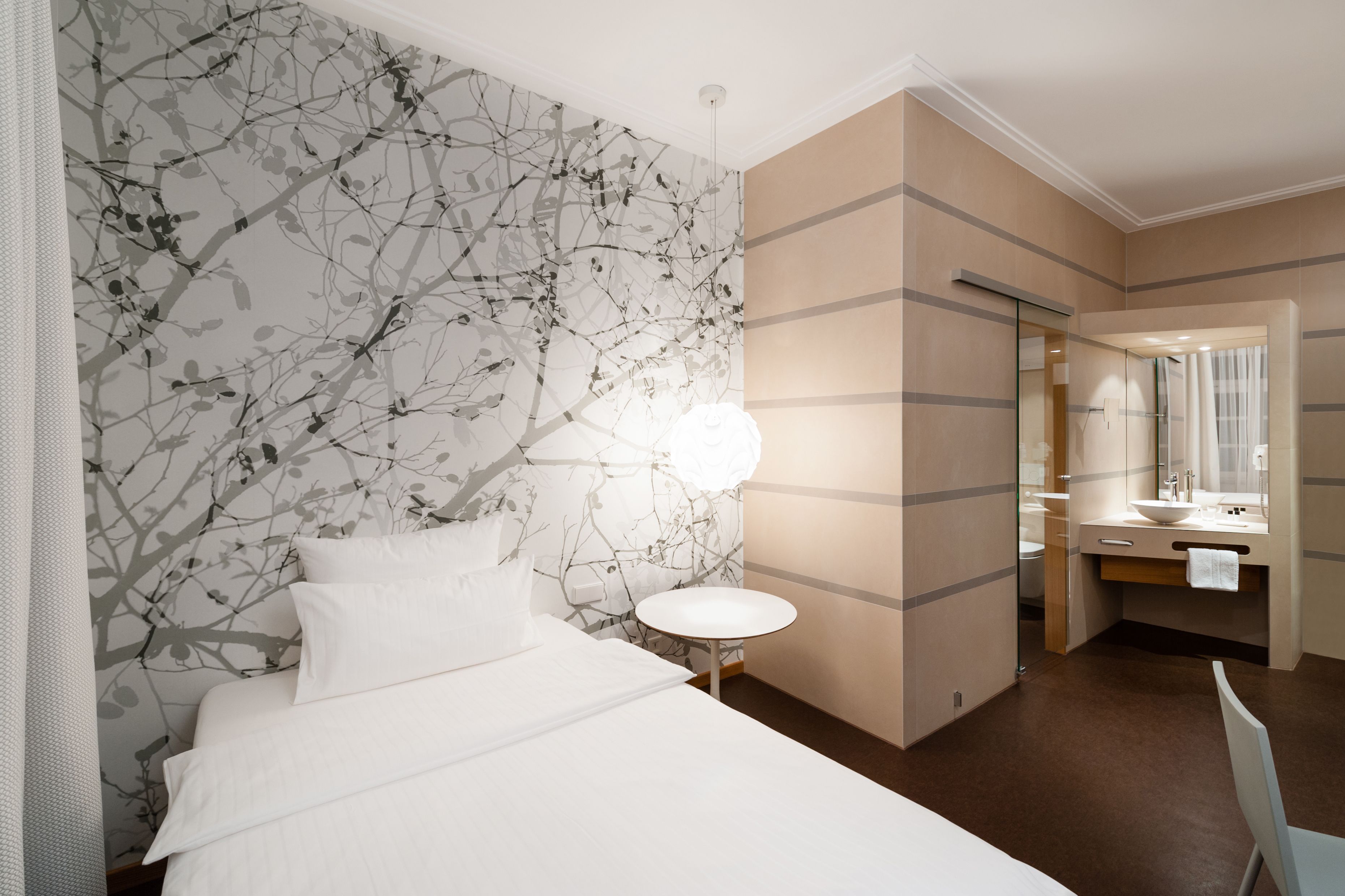 A hotel room with a bed, a round table, a mirror, and a bathroom visible through an open door.