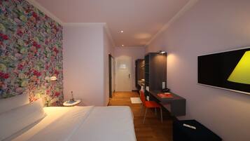 Habitació d'hotel amb un llit, un escriptori amb una cadira, un mirall, una televisió i una paret amb paper pintat floral.