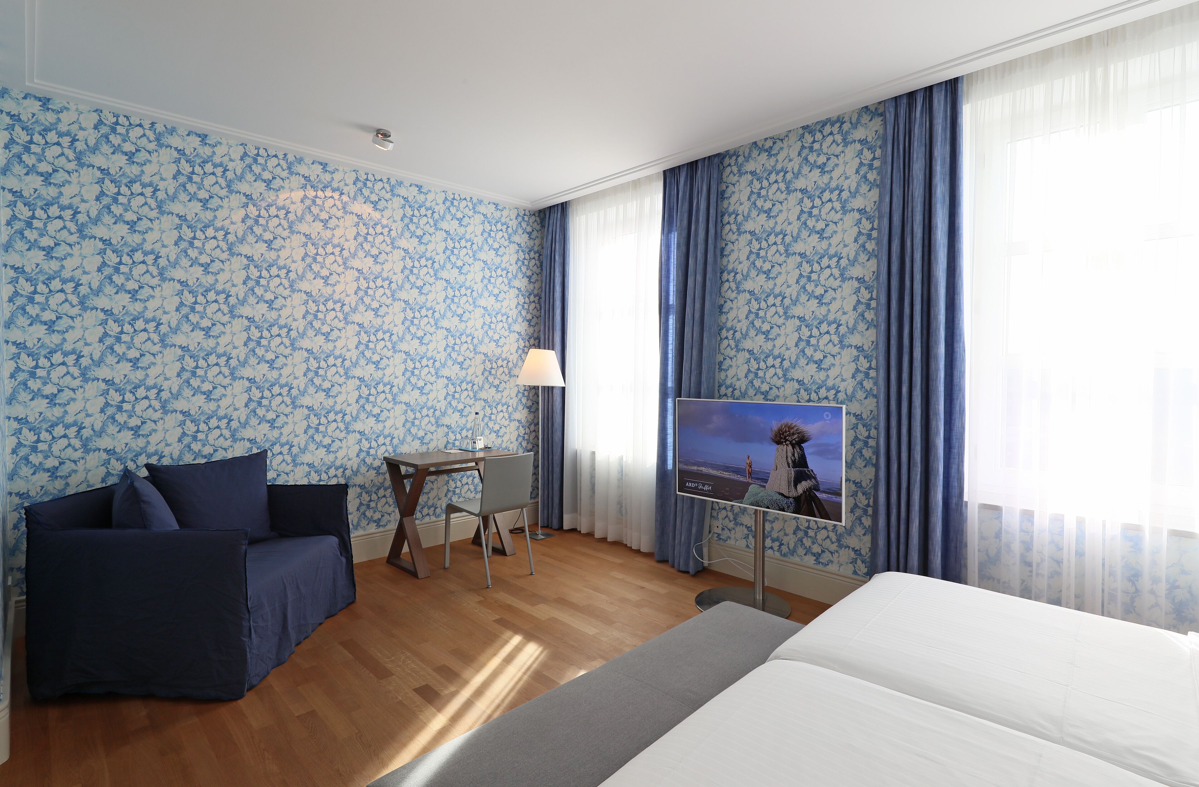 A hotel room with a large bed, a sofa, a desk, and a TV.