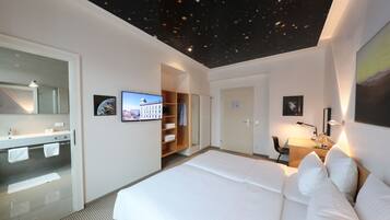 A hotel room with a bed, a desk, a wardrobe, a bathroom, and a starry ceiling.