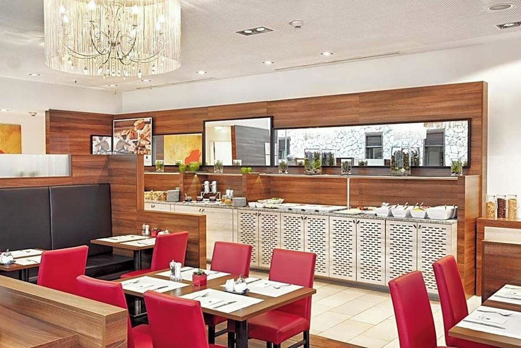 A modern restaurant interior with wooden panel walls, red upholstered seating, and a central buffet area.
