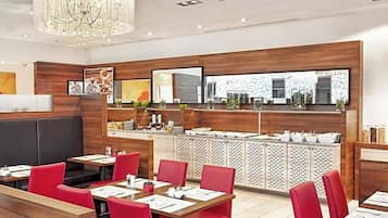 A modern restaurant interior with wooden panel walls, red upholstered seating, and a central buffet area.