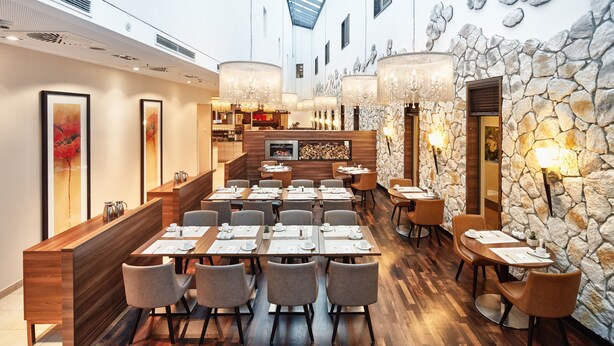Um restaurante com uma extensa área de refeições comunitária, mesas individuais e uma parede de destaque em pedra.
