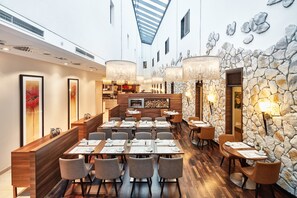 A restaurant with a long communal dining area, individual tables, and a stone accent wall. - Hotel Münster-Altstadt (Münster)