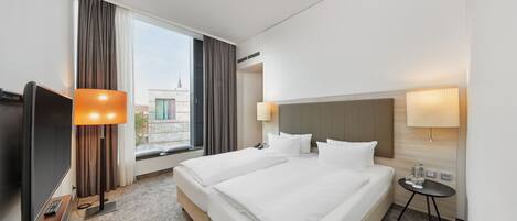 Habitación de hotel con una cama grande, dos mesitas de noche, un televisor y una ventana con cortinas.
