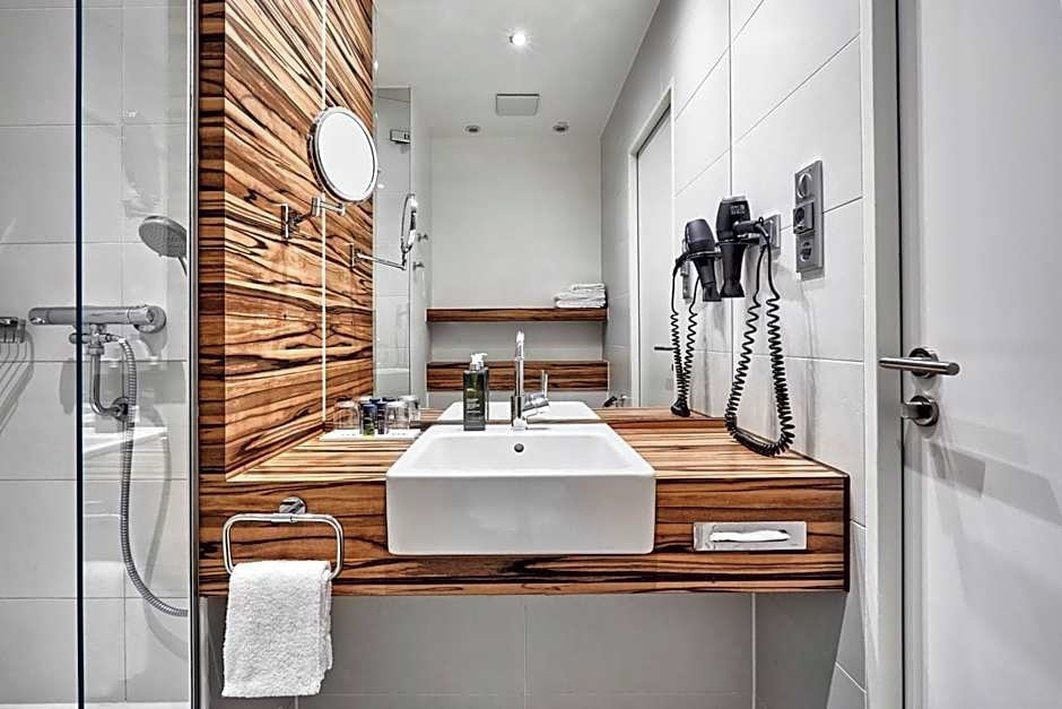A modern bathroom with a wooden vanity, a large mirror, a sink, and a hairdryer on the wall.