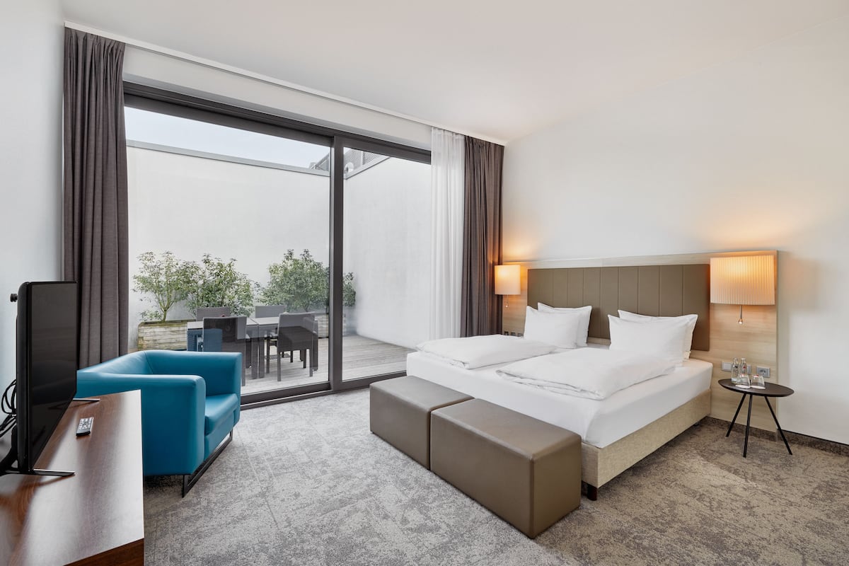 A hotel room with a large bed, a sofa, a TV, and a balcony with outdoor furniture.
