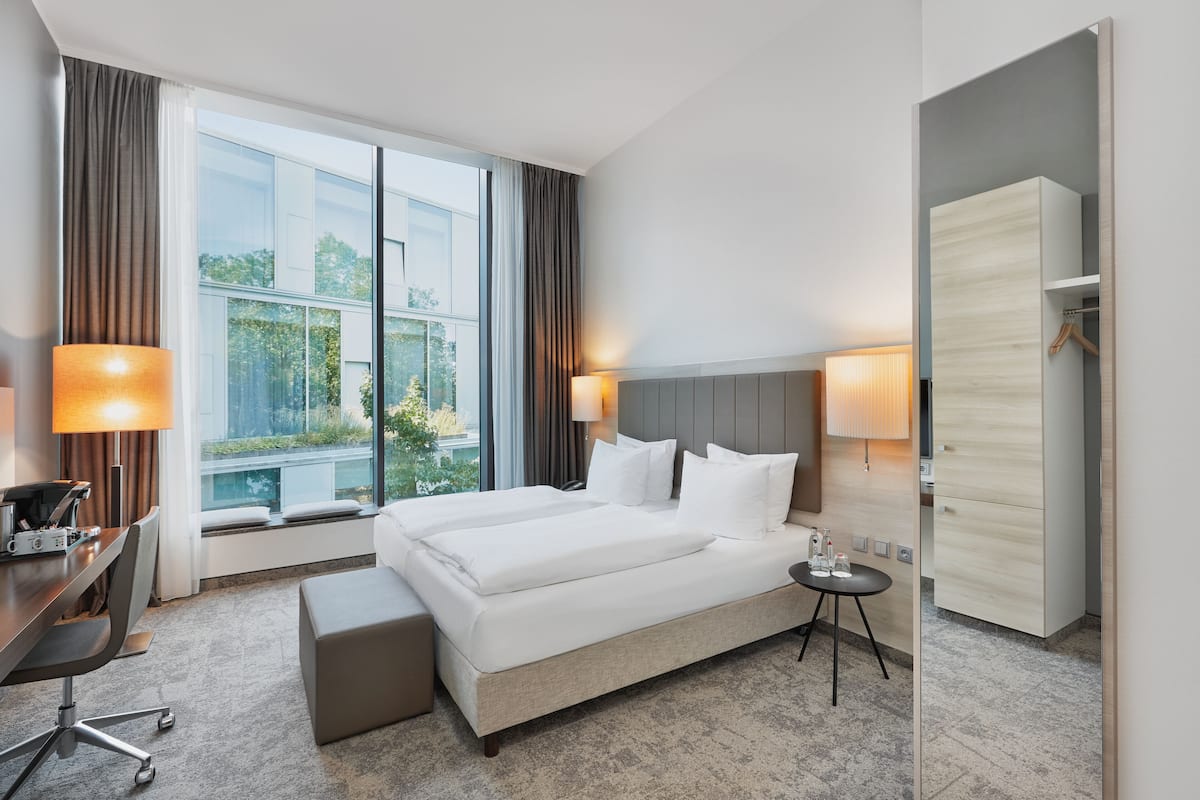 A hotel room with a large bed, a desk, a chair, a small table, and a wardrobe.