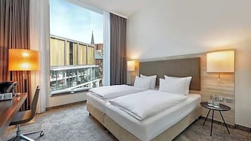 Ein Hotelzimmer mit einem großen Bett, einem Schreibtisch und Blick auf die Stadt.