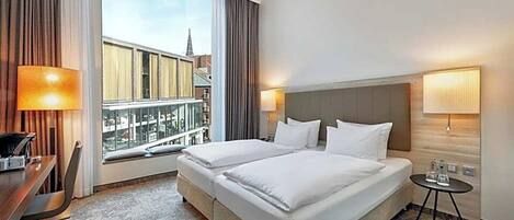 Habitación de hotel con una cama grande, un escritorio y vistas a la ciudad.