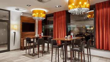 A modern dining area with wooden tables and chairs, red curtains, and chandeliers.