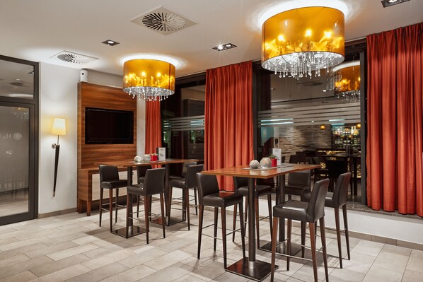 A modern dining area with wooden tables and chairs, red curtains, and chandeliers. - Hotel Münster-Altstadt (Münster)