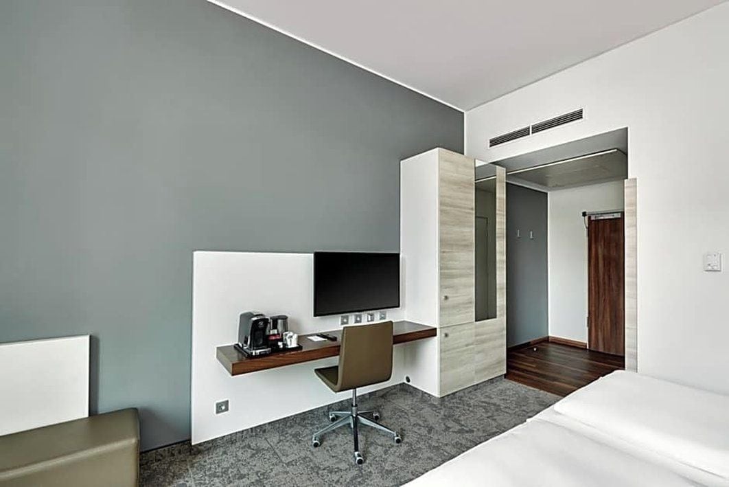 Une chambre d’hôtel moderne équipée d’un lit, d’un bureau avec une chaise, d’un téléviseur à écran plat et d’un miroir.