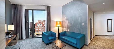 A hotel room with a large window, a sofa, a coffee table, and a lamp.