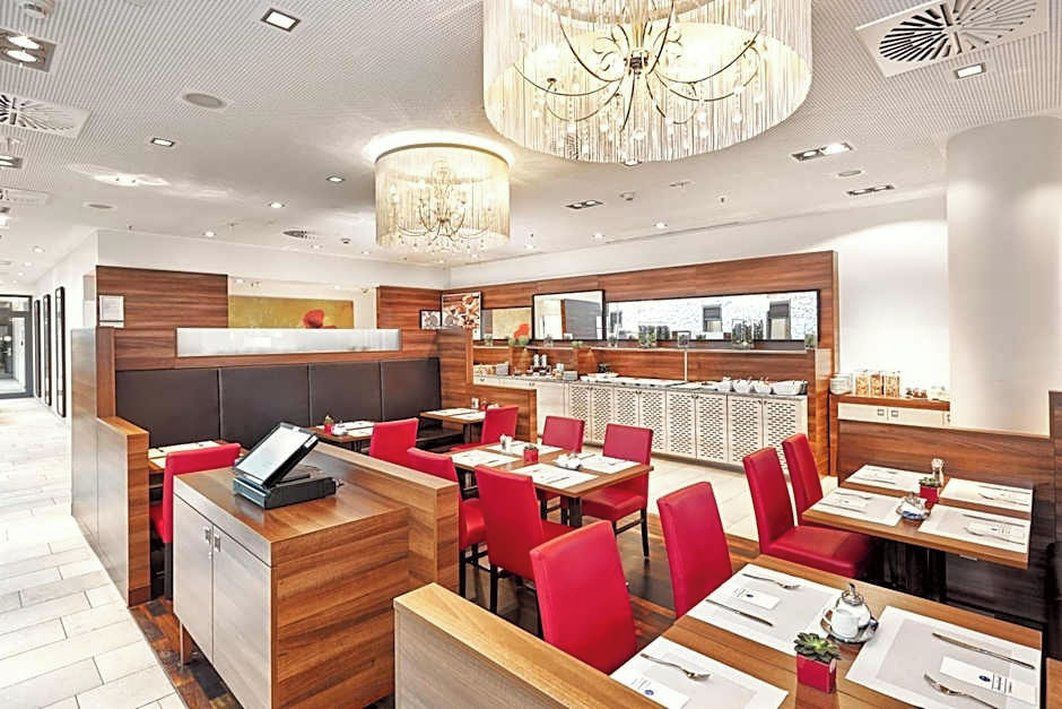 Interior moderno de restaurante con paneles de madera, asientos tapizados en rojo y una zona de bar central.
