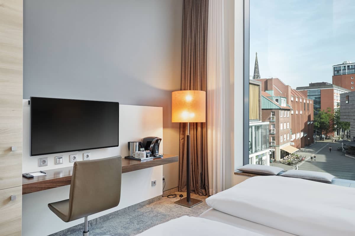 A hotel room with a flat-screen TV, a desk with a coffee maker, a lamp, and a bed.