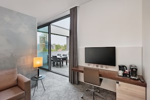 A hotel room with a desk, chair, TV, lamp, coffee maker, and a view of the outside. - Hotel Münster-Altstadt (Münster)