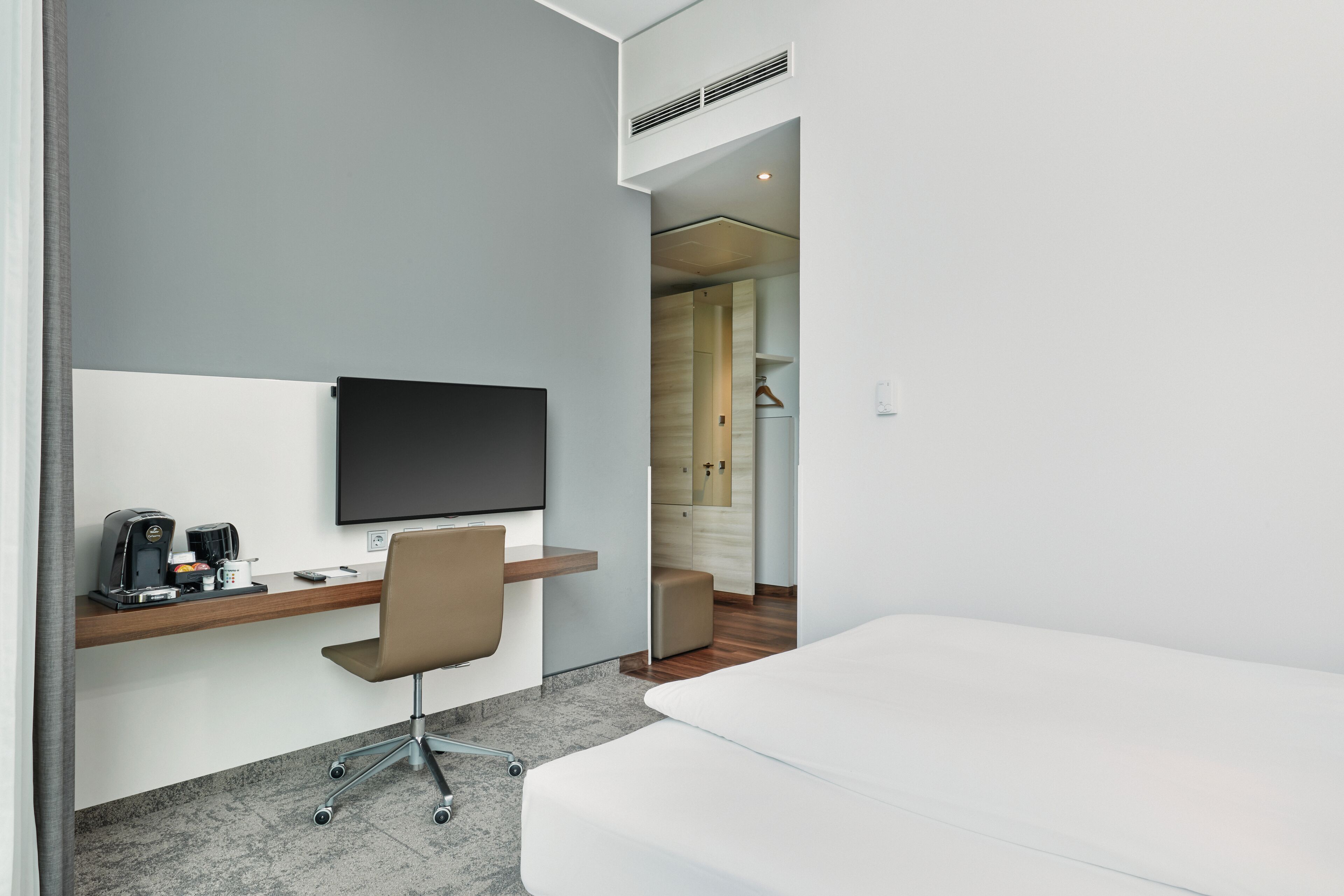 Une chambre d’hôtel moderne équipée d’un téléviseur à écran plat fixé au mur, d’un bureau avec une chaise, d’un lit et d’un petit coin salon avec un canapé.