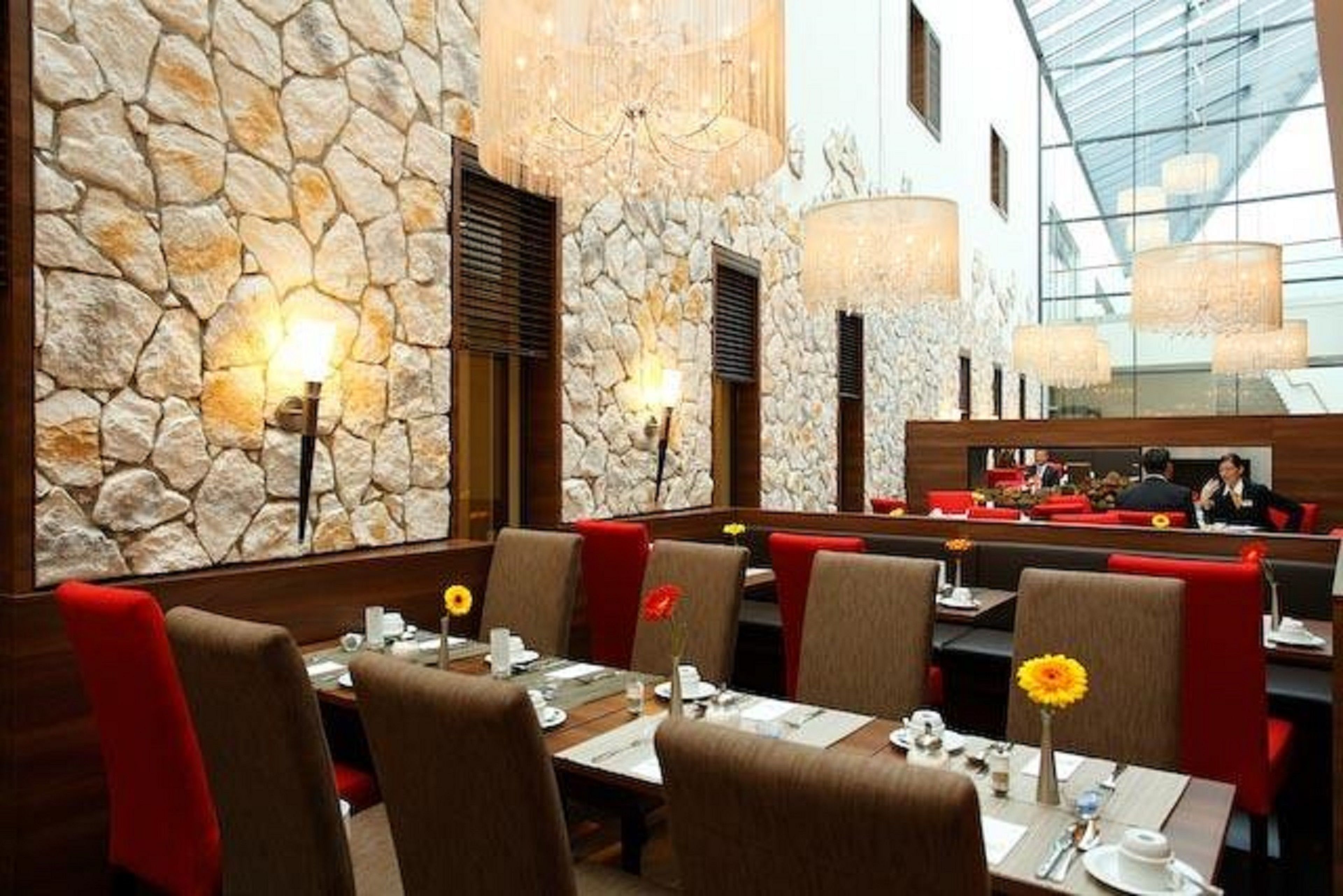 Ein Restaurant mit Steinsälen, roten Polstersitzen und einer hohen Decke mit Kristalllüstern.