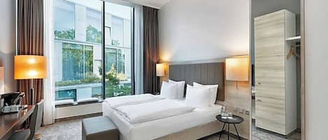 Una habitación de hotel con una cama grande, mesitas de noche, un escritorio y un armario.