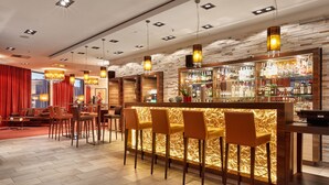 Uma área de bar com balcão de madeira, vários bancos altos e iluminação pendente.