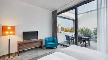 A hotel room with a large bed, a flat-screen TV, a desk, a chair, and a balcony with a table and chairs.