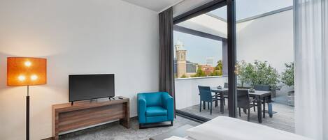 Habitación de hotel con una cama grande, televisión de pantalla plana, escritorio, silla y balcón con mesa y sillas.