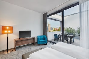 A hotel room with a large bed, a flat-screen TV, a desk, a chair, and a balcony with a table and chairs. - Hotel Münster-Altstadt (Münster)