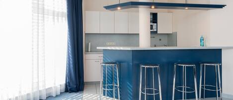 Una cocina moderna con una isla central, taburetes de bar y un ventanal con cortinas.