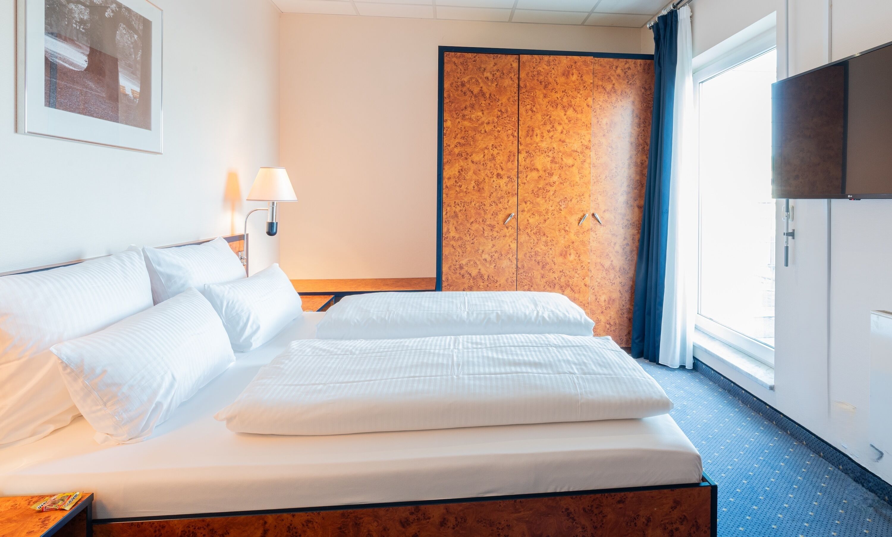 A hotel room with a bed, a wardrobe, a TV, and a window.