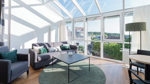 Een moderne woonkamer met een glazen dak, een grijze bank, een salontafel en uitzicht op de stad.
